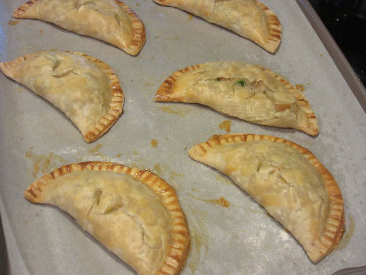 Six baked chicken pot pie crust pockets on a baking sheet with parchment paper.