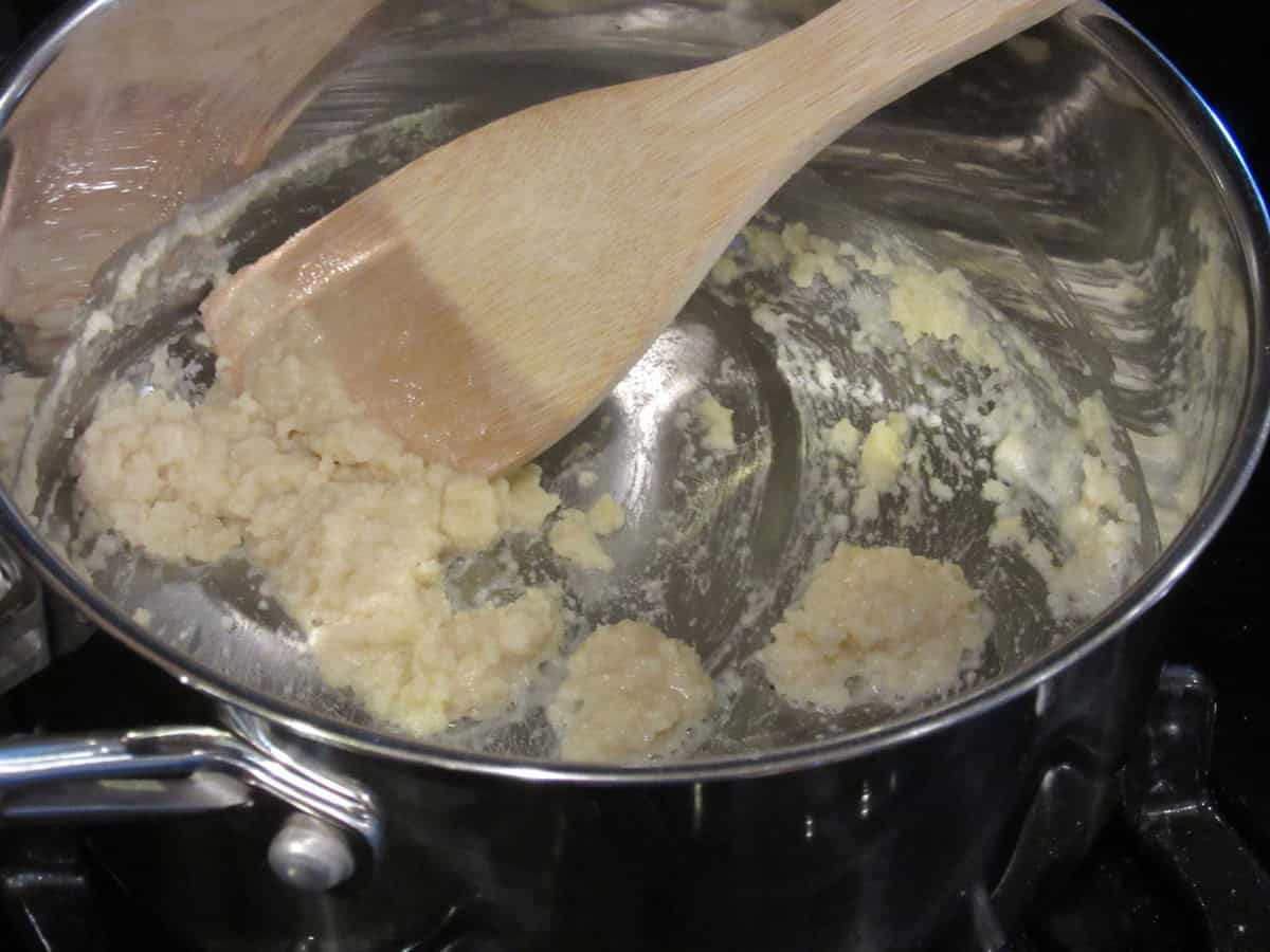 A flour and butter roux in a pot on the stovetop with a wooden spoon.