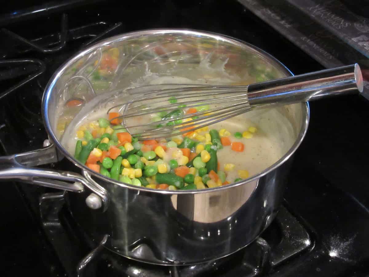 Colorful mixed vegetables added into a stockpot with a thickened chicken stock.