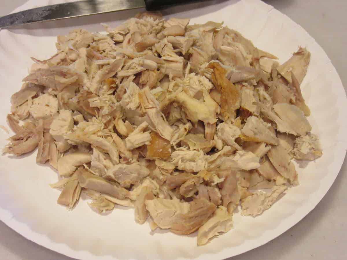 A paper plate filled with chicken pieces taken from a rotisserie chicken.