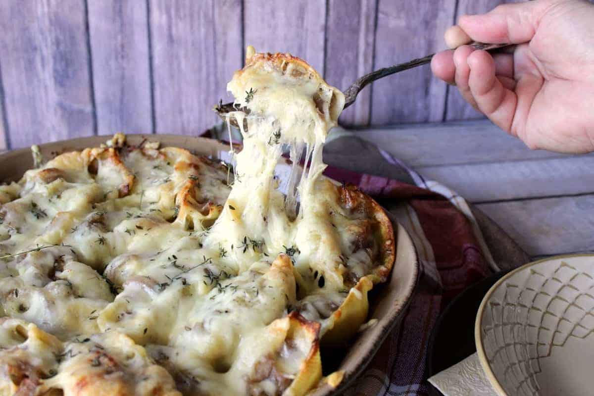A melted cheese pull serving up French onion stuffed shells from a casserole dish.