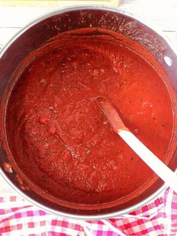 A large saucepan filled with homemade marinara sauce sitting on top of a red and white checkered napkin.
