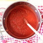 A look inside a large saucepot containing homemade marinara sauce along with a wooden spoon.
