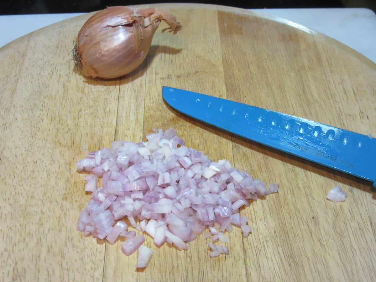 Minced shallots on a cutting board with a knife.