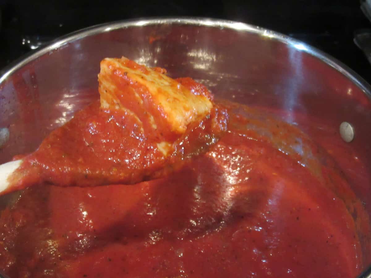 The spent rind of Parmesan cheese being removed from a pot of marinara sauce.