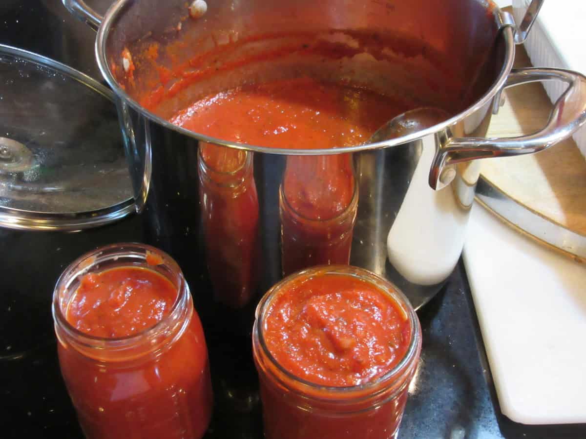 A large saucepan and two mason jars filled with homemade marinara sauce.