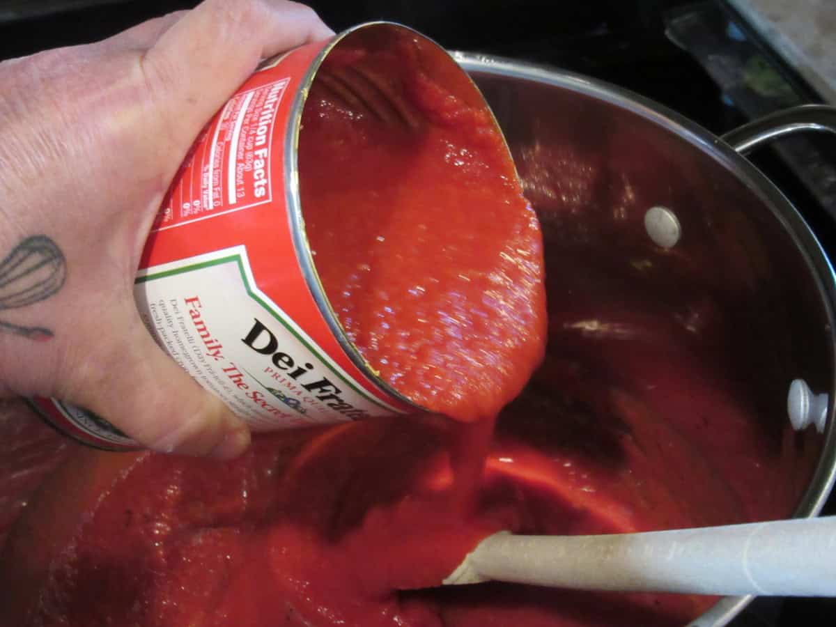 A can of crushed tomatoes being added to a large saucepan.