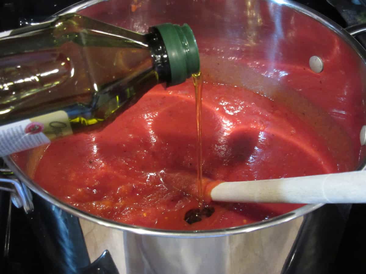 Olive oil being added to a saucepan of homemade marinara sauce.