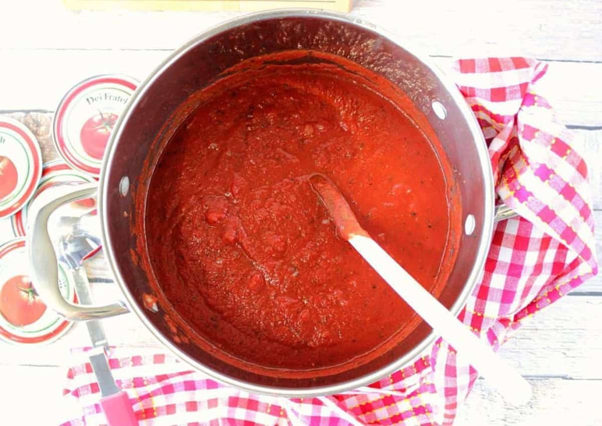 A large saucepot filled with homemade marinara sauce sitting on a red and white checked napkin.