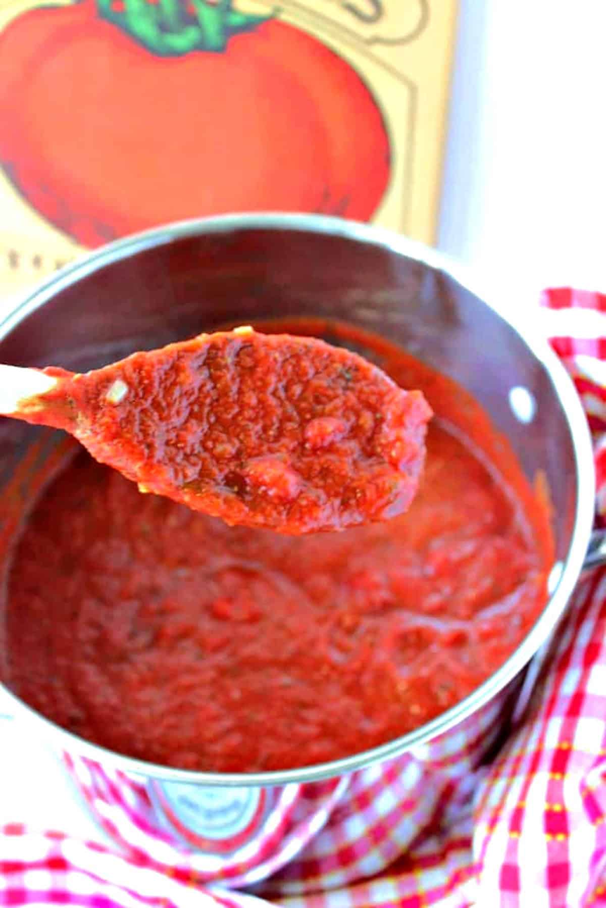 A wooden spoon showing the texture of a homemade marinara sauce over a saucepan.