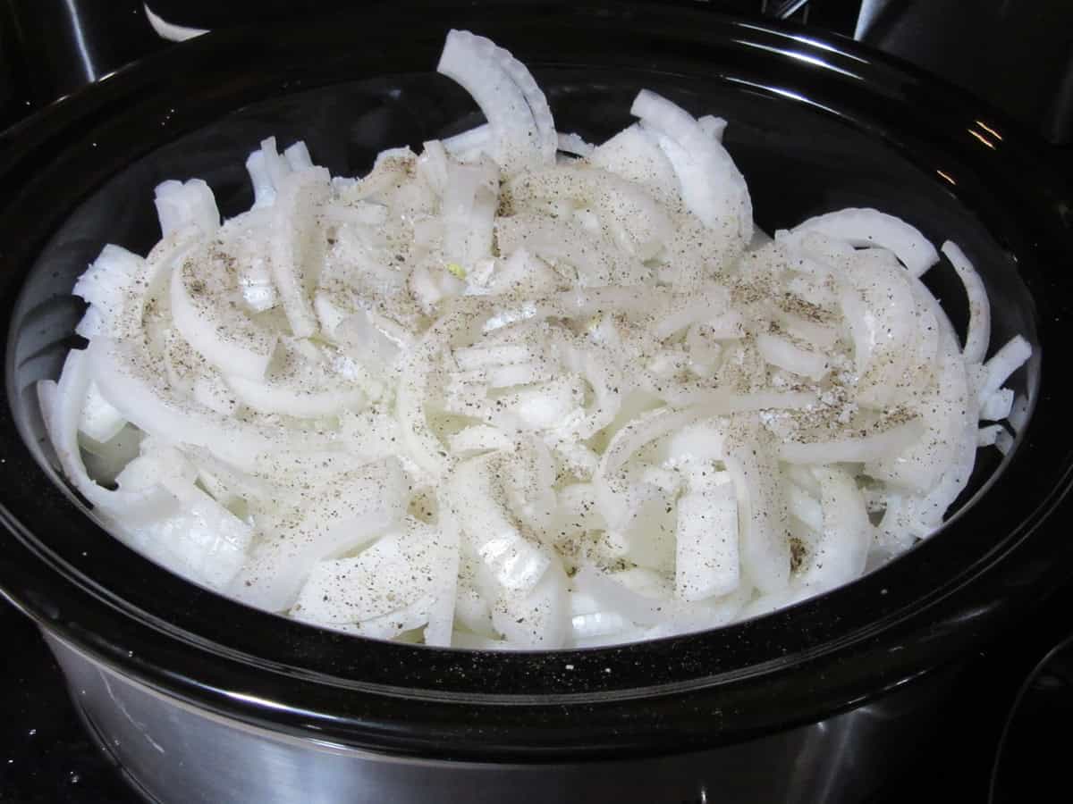Sliced onions, salt and pepper in a slow cooker.