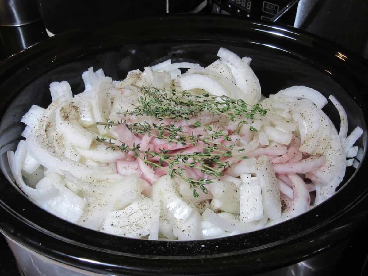 Sliced onions, red wine, pepper, and fresh thyme in a slow cooker.