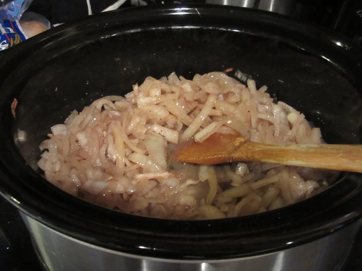 A slow cooker filled with red wine caramelized onions.