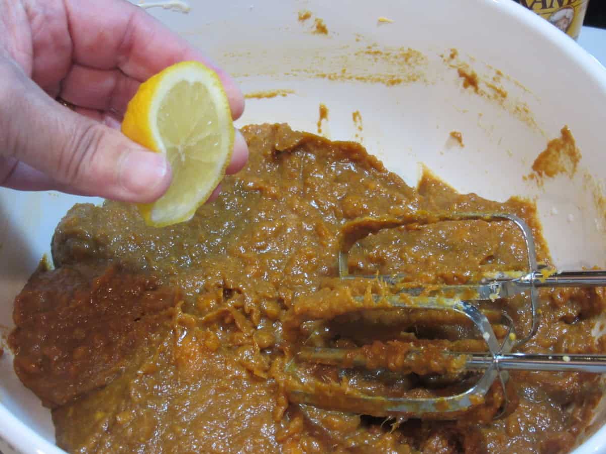 A squeeze of lemon being added into a sweet potato cookie dough in a white bowl.