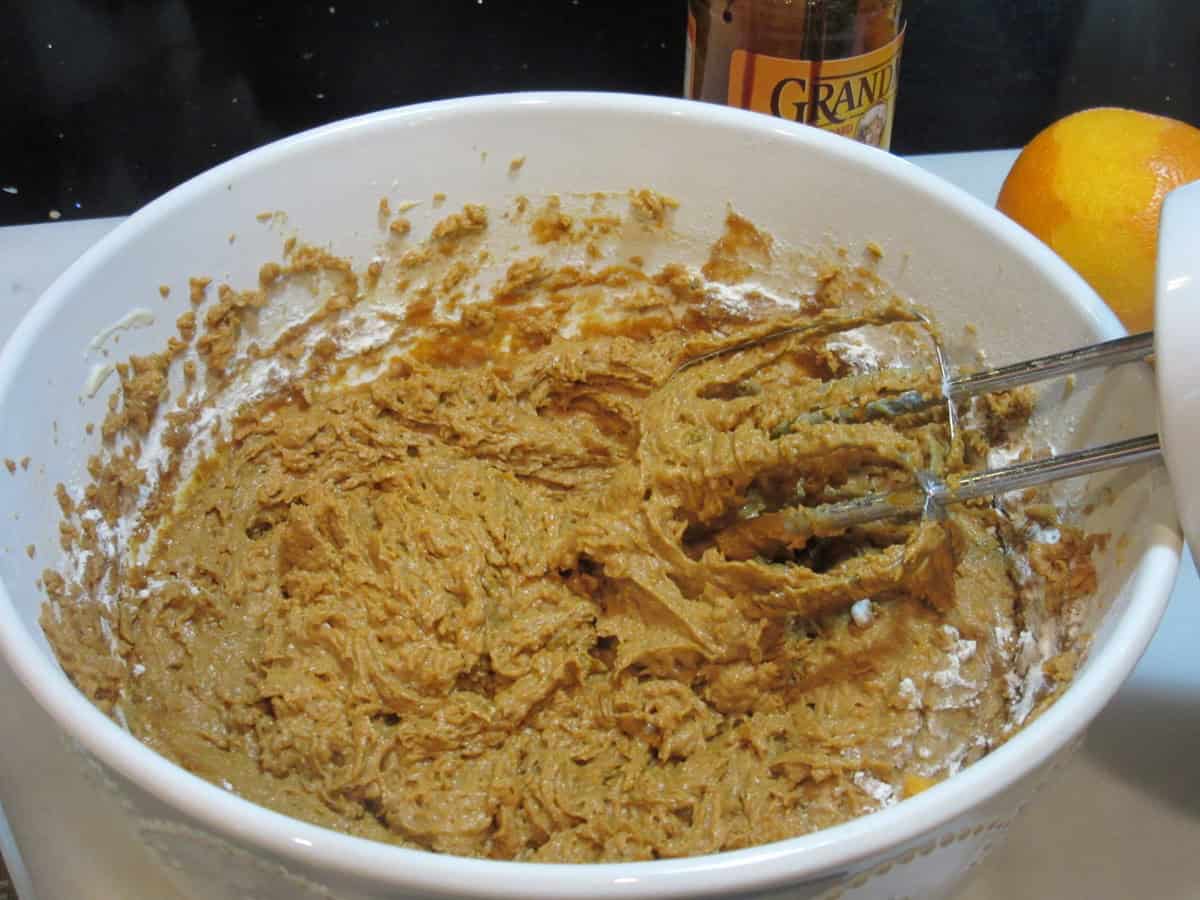 A hand mixer in a white bowl blending a sweet potato cookie batter.