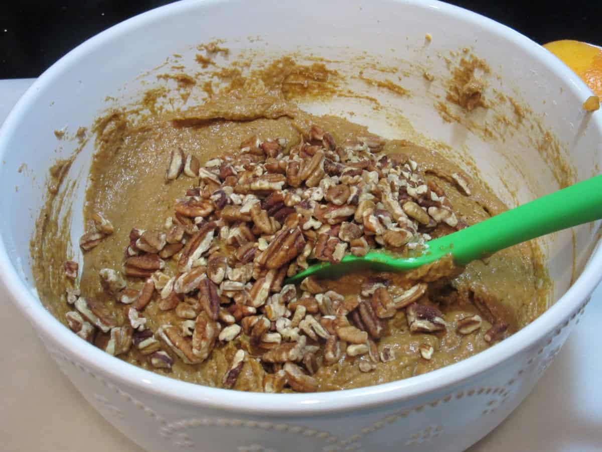 A white bowl filled with sweet potato cookie batter and chopped pecans.