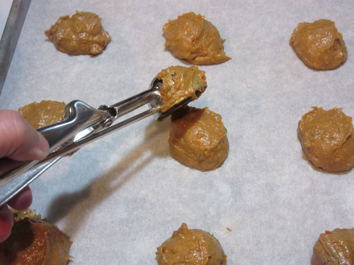 A cookie scoop scooping out sweet potato cookie dough onto a baking sheet.