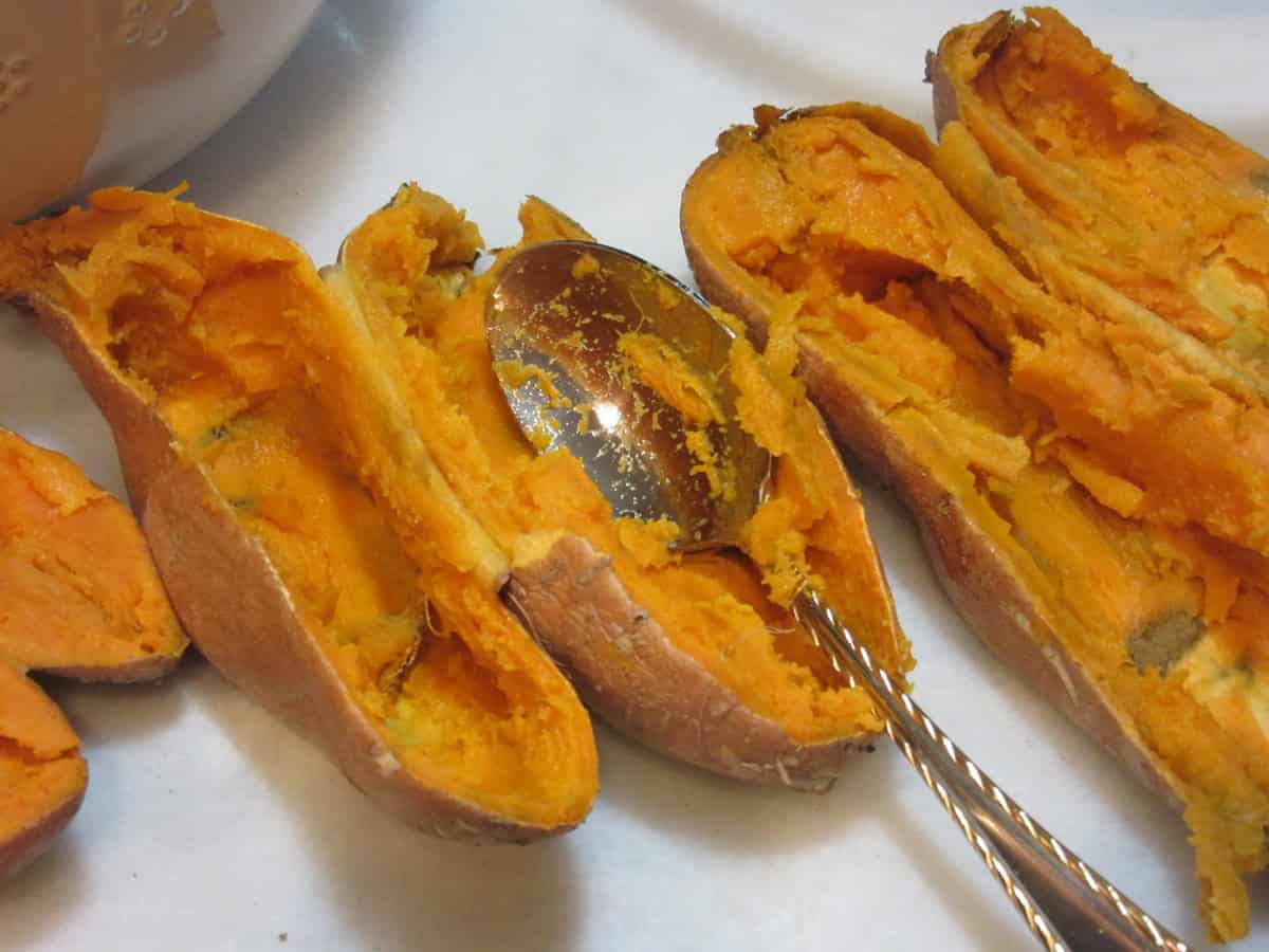 A spoon scooping out the soft centers of baked sweet potatoes.