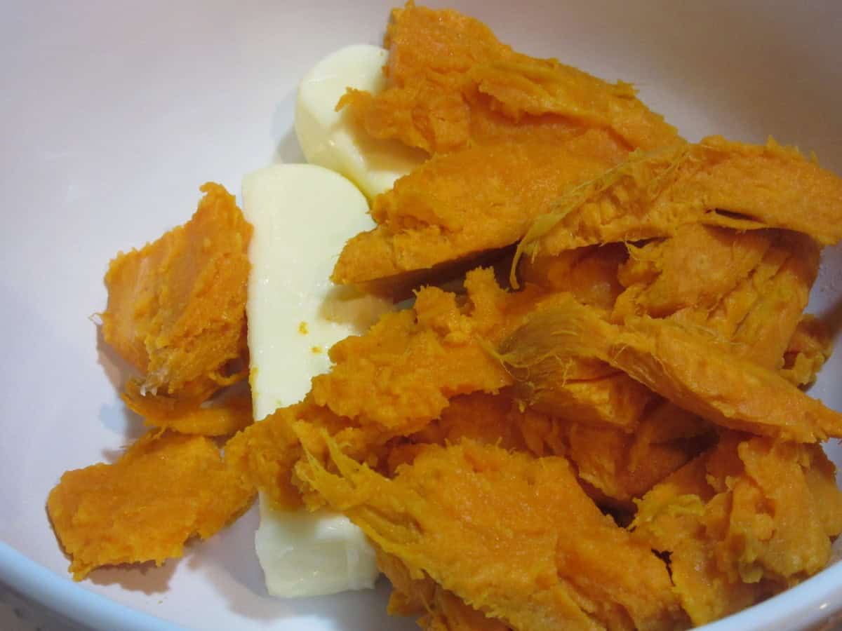Cooked sweet potatoes and sticks of butter in a large white bowl.