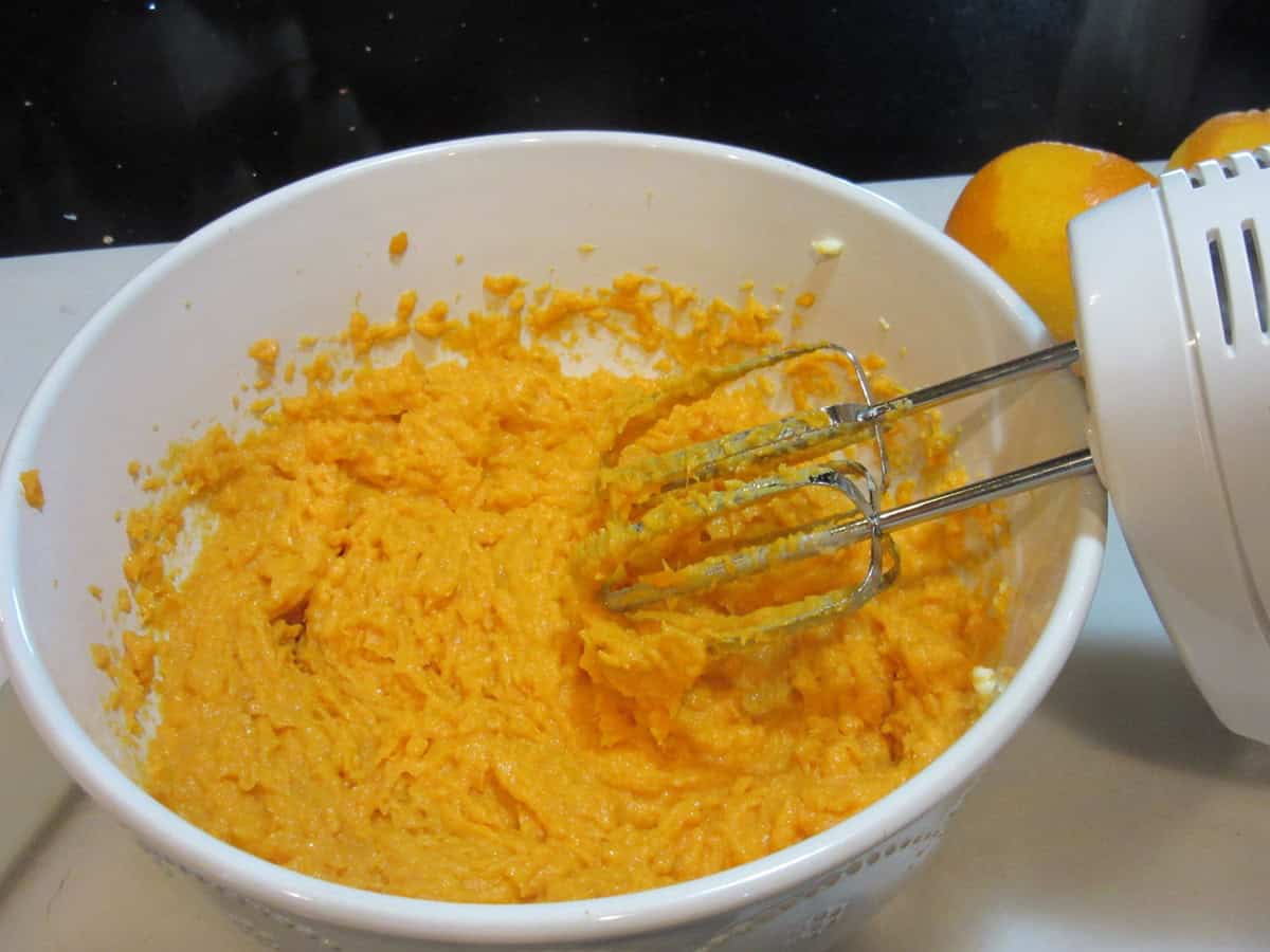 Mashed sweet potatoes, eggs and sugar blending in a large white bowl.