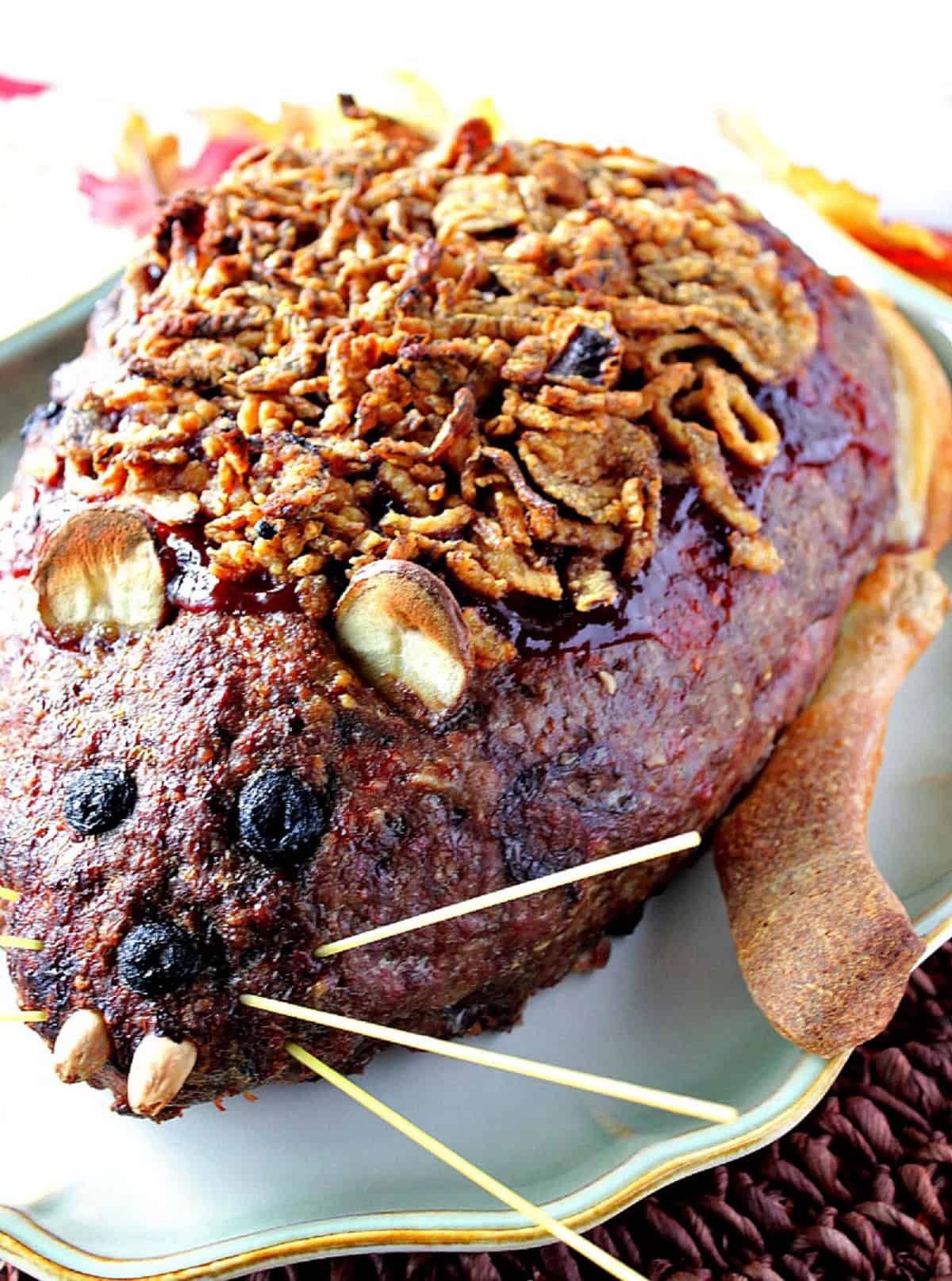 A fully baked, creepy looking rat loaf meatloaf with French fried onion fur on a platter for Halloween dinner.