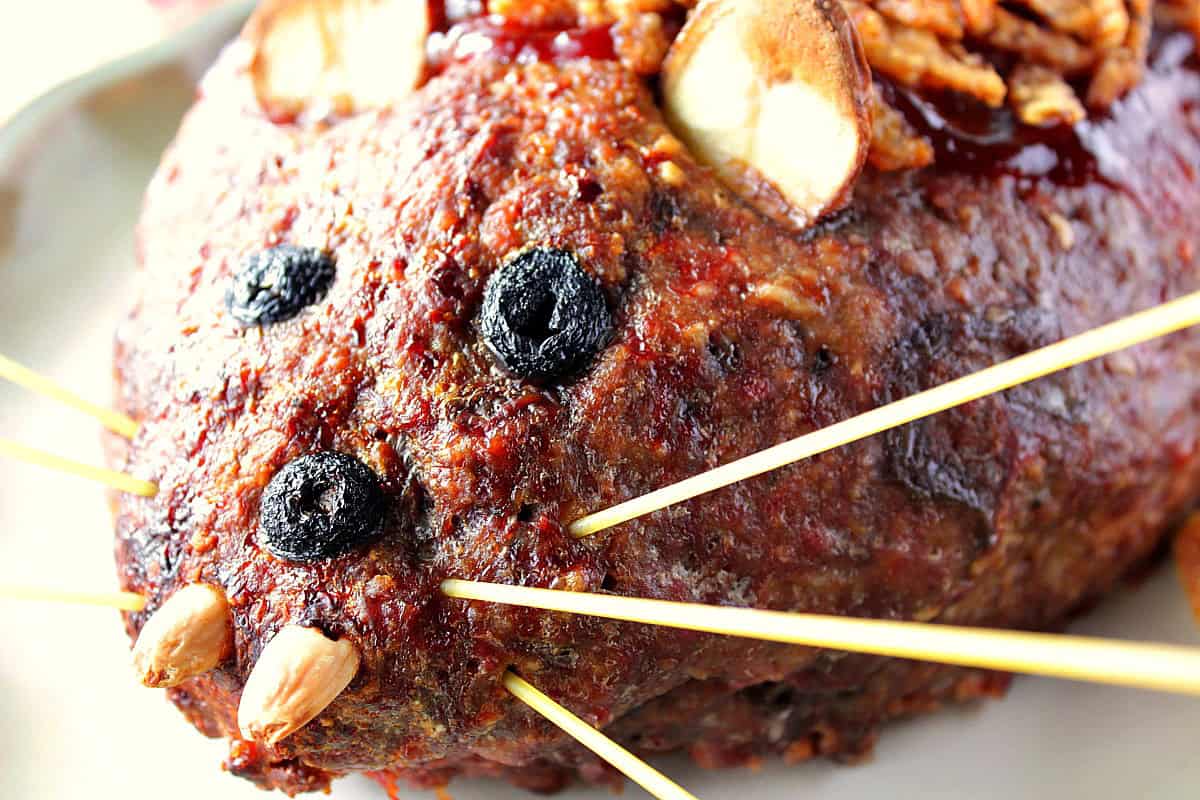 Olive eyes, almond teeth and spaghetti whiskers finish off a baked rat loaf meatloaf for Halloween dinner.