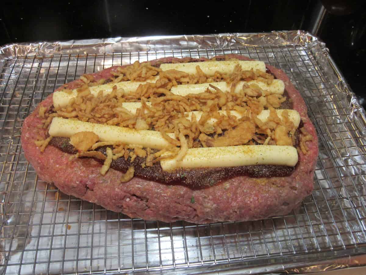 BBQ sauce, string cheese and French fried onions on top of a cone-shaped unbaked meatloaf layer.