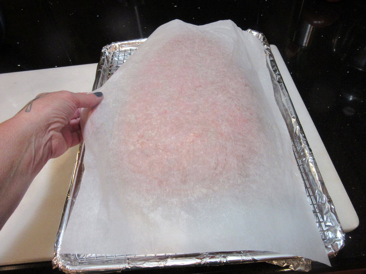 A sheet of parchment paper being removed from a rat loaf meatloaf after turning the meatloaf out.