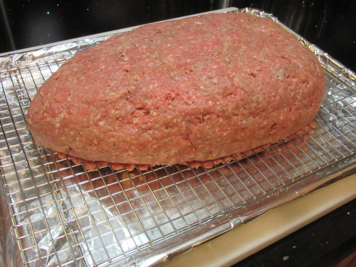 A large unbaked rat loaf meatloaf on a baking rack with aluminum foil.