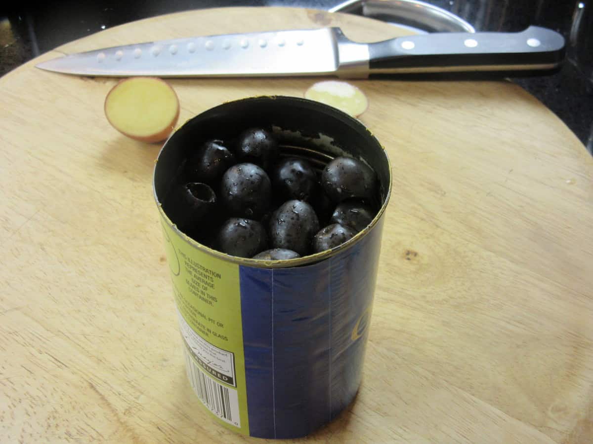 A drained can of black olives on a cutting board.