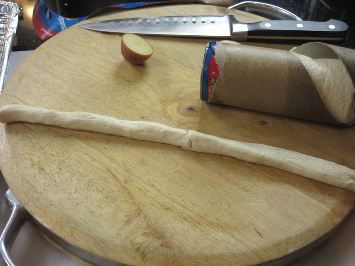 Two unbaked biscuit ropes being added together on a cutting board.