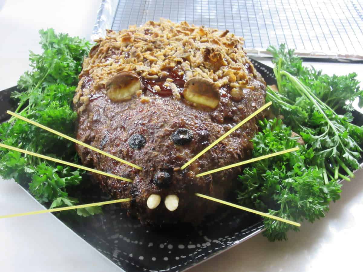 A fun and creepy baked rat loaf meatloaf on a platter surrounded by fresh parsley.
