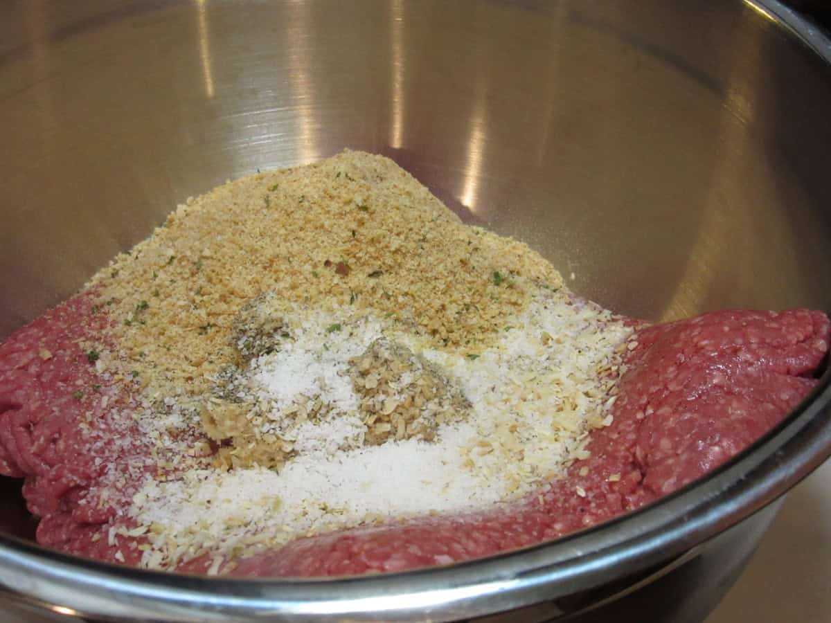 Ground meat, breadcrumbs and seasonings in a silver bowl before mixing to make meatloaf.
