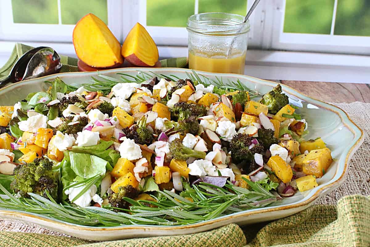 A platter filled with a colorful green and golden roasted golden beet and broccoli salad with rosemary and goats cheese.
