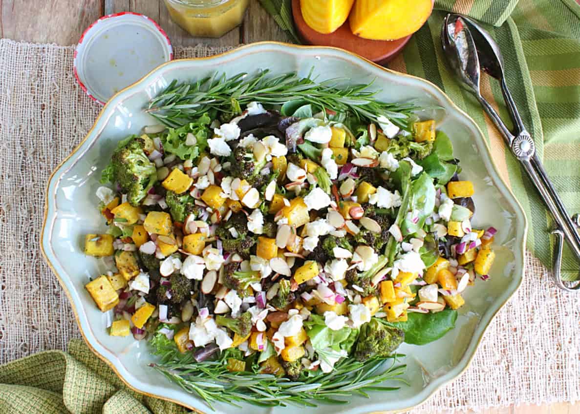 An overhead photo of a platter of green and gold beet and broccoli salad with lettuce, red onion, goat cheese and almonds.