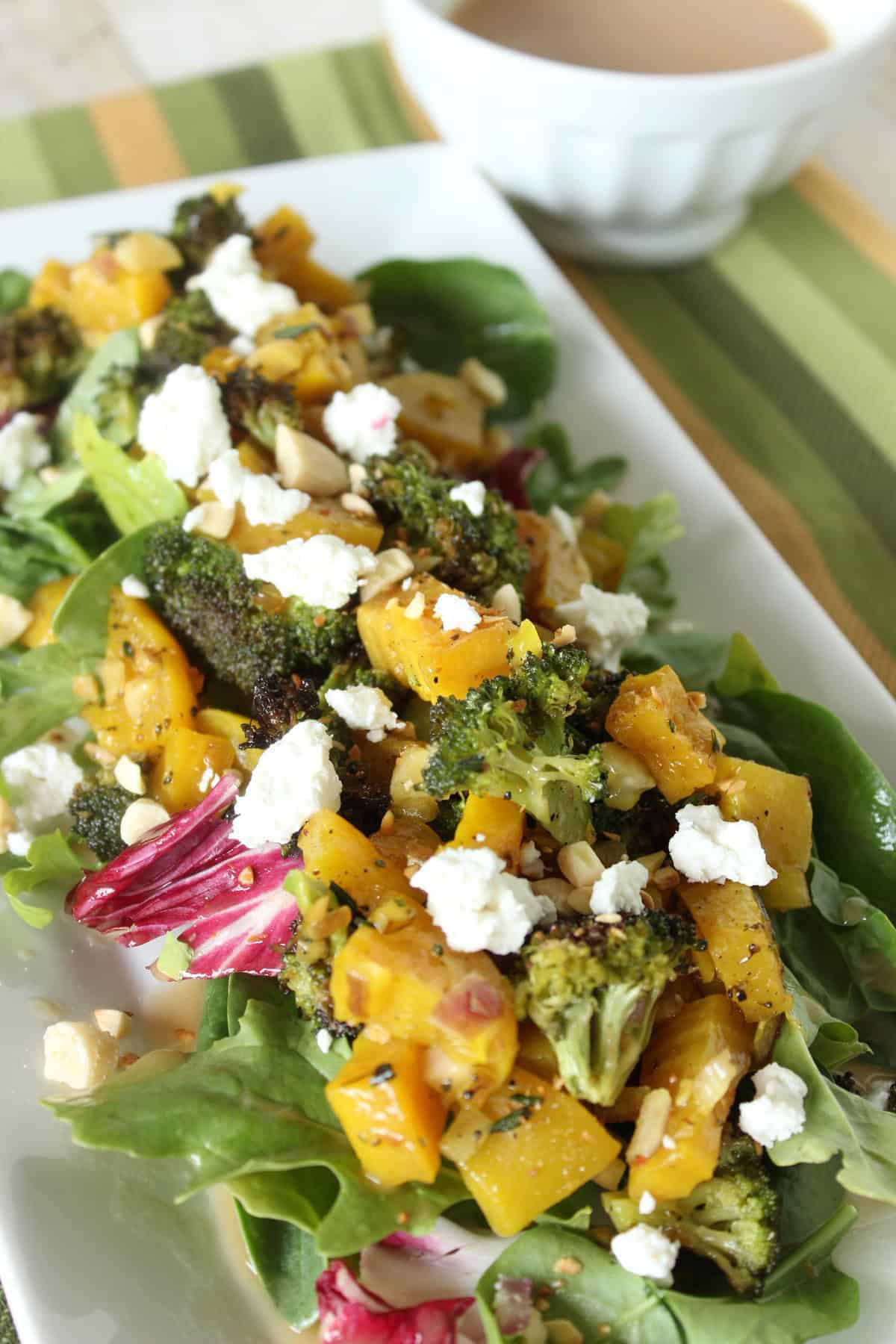 A white rectangle plate holding a roasted golden beet and broccoli salad topped with goat cheese.