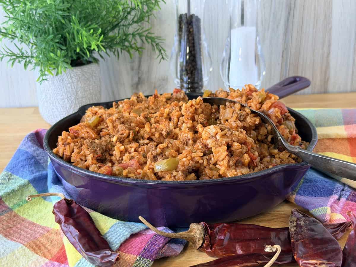 A purple skillet filled with Spanish rice with a serving spoon inside.