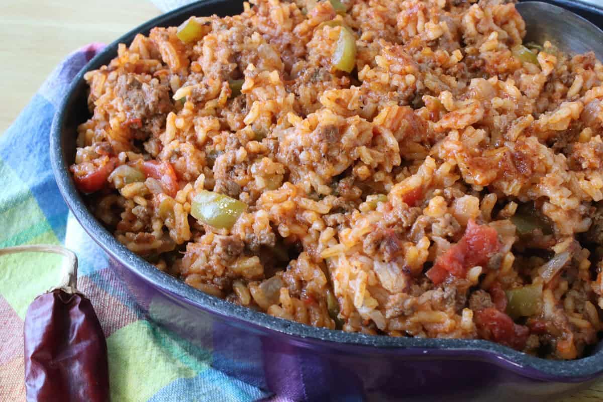 A closeup of rice, tomatoes, ground beef and pepper casserole in a purple skillet.