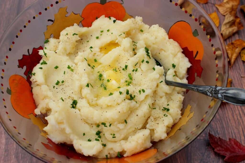 A perfect looking bowl of mashed potatoes topped with chives and melted butter.