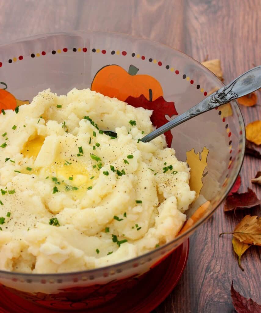 A autumn glass bowl filled with mashed potatoes and celery root along with a serving spoon.