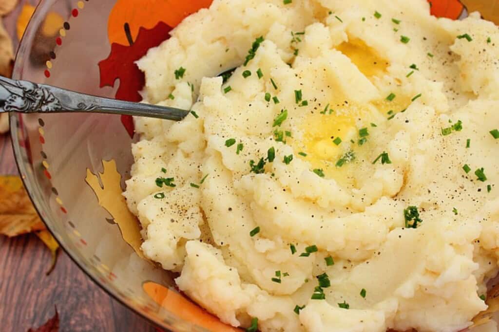 A serving spoon in a pile of buttery mashed potatoes and celery root.