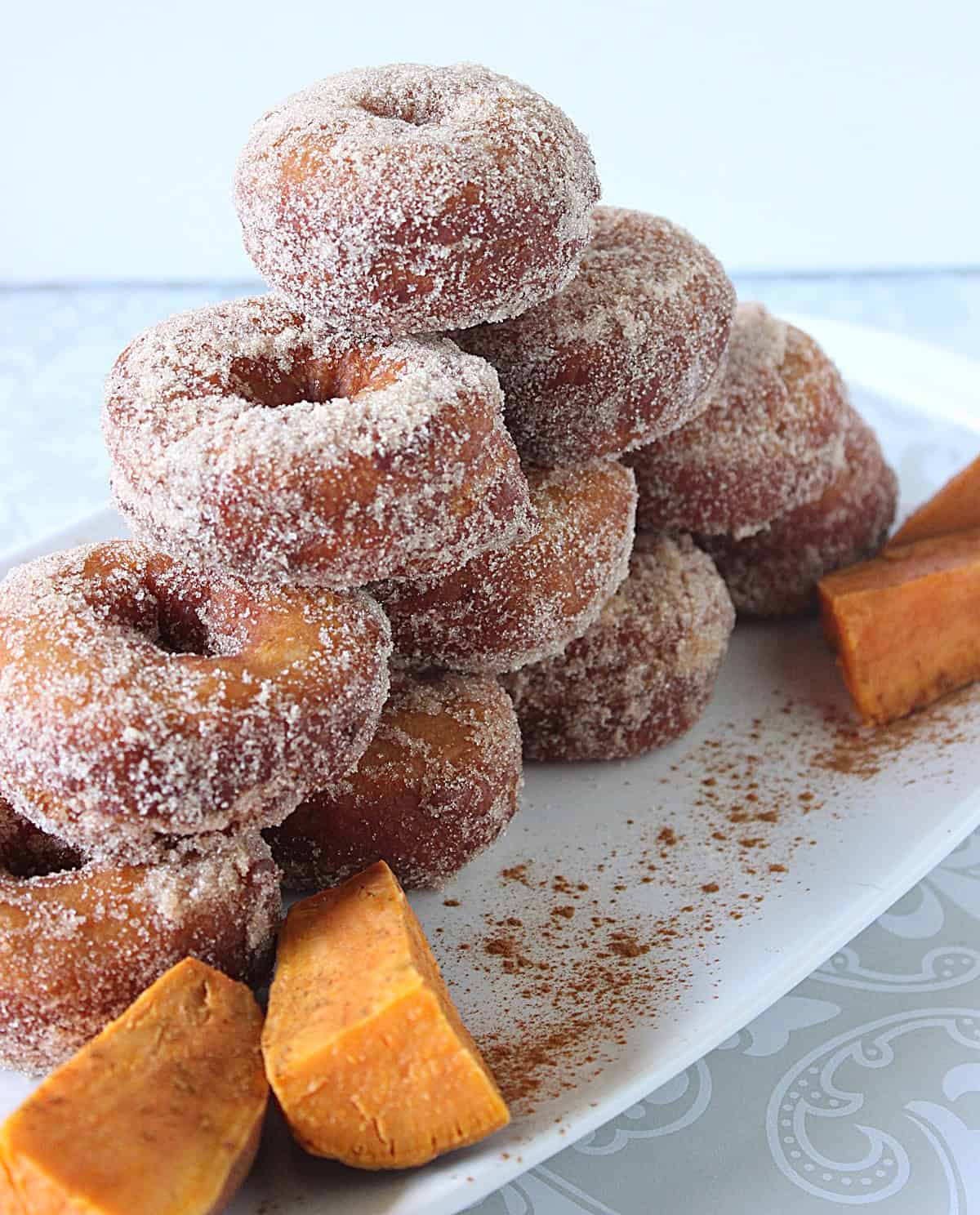 A tall stack of yummy looking cinnamon sugar topped sweet potato donuts made from mashed sweet potatoes.
