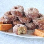 A platter of sweet potato donuts dipped in cinnamon sugar with one in the front with a bite taken out.