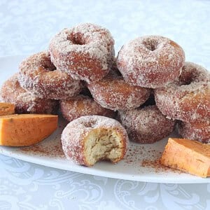 A platter of sweet potato donuts dipped in cinnamon sugar with one in the front with a bite taken out.