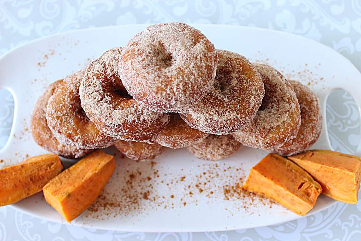 A stack of 10 sweet potato cake donuts on a white platter with sweet potato wedges.