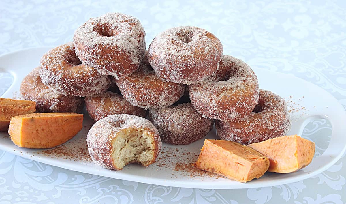 A white plate topped with a stack of sweet potato donuts topped with cinnamon sugar.