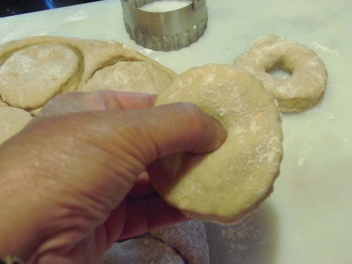 A thumb poking a hole through a dough circle to make donuts.
