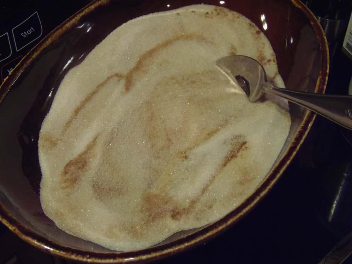 A bowl with a mixture of sugar and cinnamon along with a spoon.