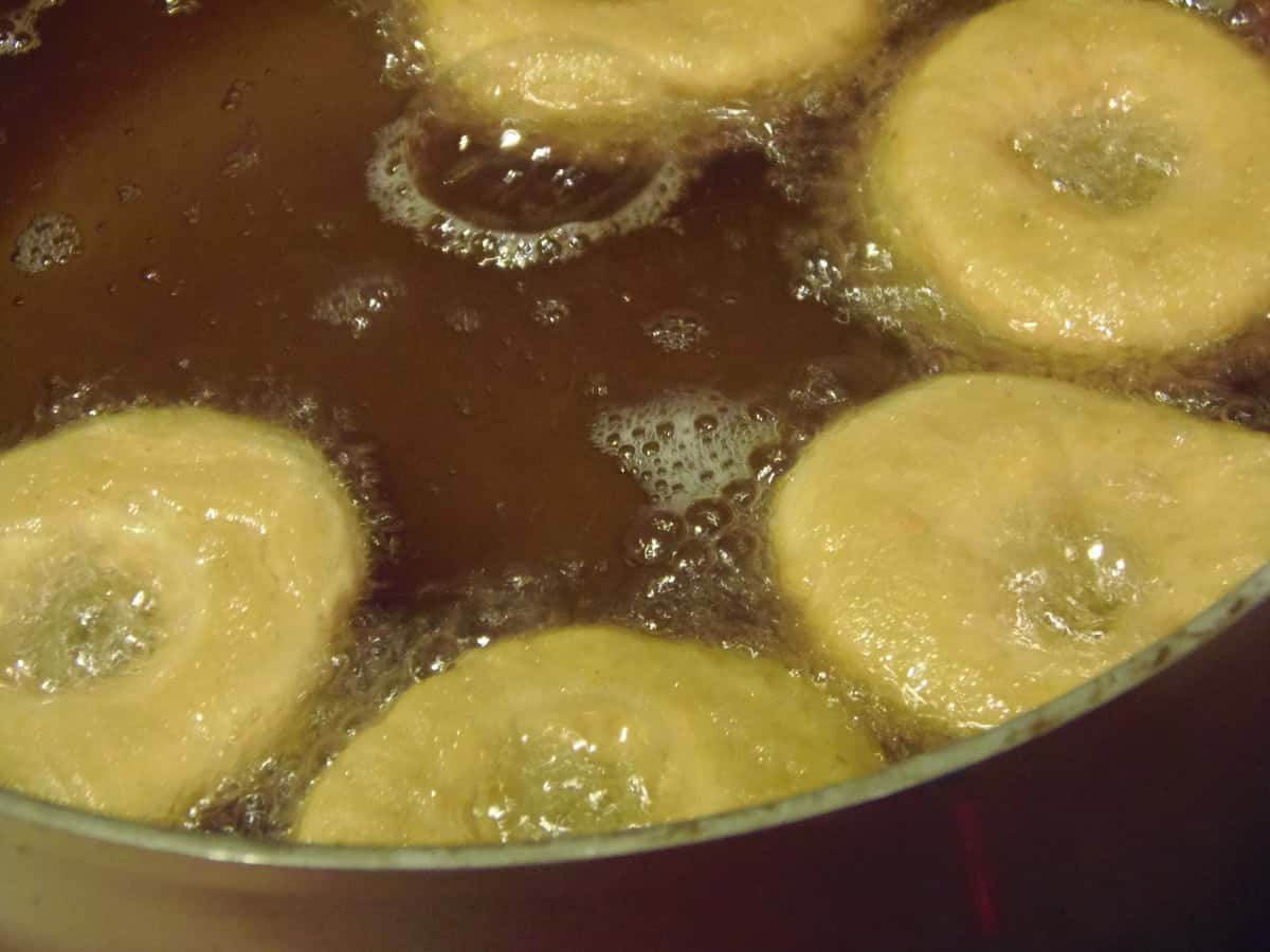 Five sweet potato cake donuts being fried in hot oil.