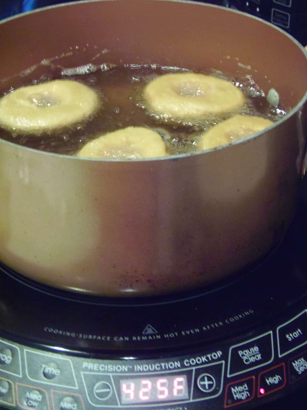 Four sweet potato cake donuts being fried in oil using an induction cooktop.